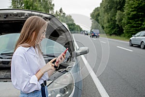 Young woman standing near broken down car with popped up hood having trouble with her vehicle. Waiting for help tow truck or