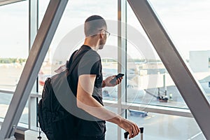 Young woman standing near window at airport holding mobile phone