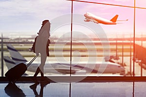 Young woman is standing near window at the airport and watching