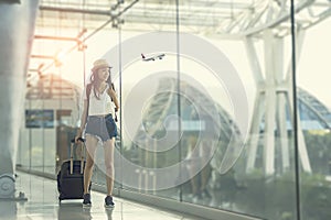 Young woman is standing near window at the airport and watching