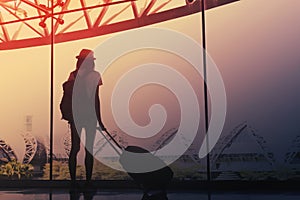 Young woman is standing near window at the airport and watching plane before departure