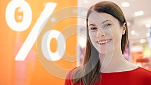 Young woman standing near window shop. Sale percent sign. Female shopper looking at window shop