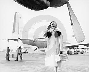 Young woman standing next to an airplane looking happy