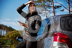 Young Woman Standing Next To Broken Down Car Trying To Get Signal On Mobile Phone