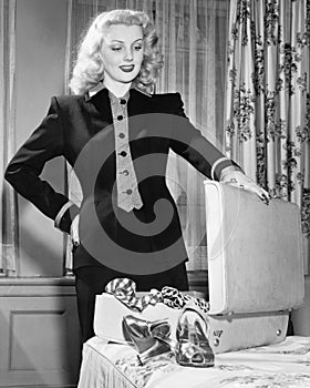 Young woman standing next to her bed, holding onto the suitcase, thinking of what to pack