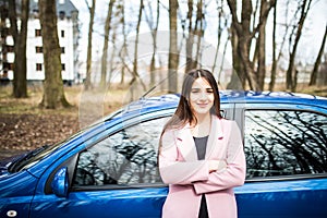 Young woman standing next to her new car with crossed hands