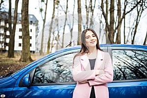 Young woman standing next to her new car with crossed hands