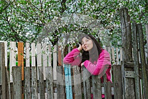 Young woman standing by old fence and dreamy looking