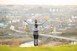 Young woman standing outdoors raising her hands enjoying city view. Relaxing, freedom and wellness concept