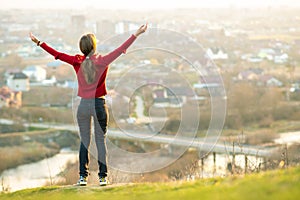 Young woman standing outdoors raising her hands enjoying city view. Relaxing, freedom and wellness concept