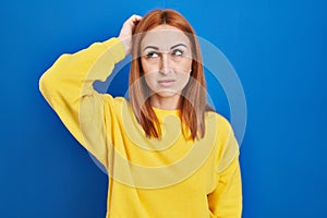 Young woman standing over blue background confuse and wondering about question