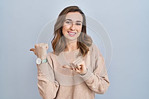 Young woman standing over isolated background pointing to the back behind with hand and thumbs up, smiling confident