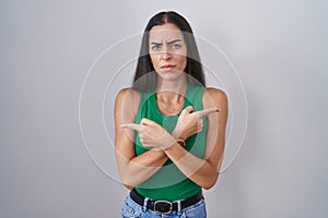 Young woman standing over isolated background pointing to both sides with fingers, different direction disagree