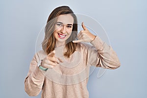 Young woman standing over isolated background smiling doing talking on the telephone gesture and pointing to you