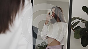 Young woman standing with phone in front of the mirror, making a photo