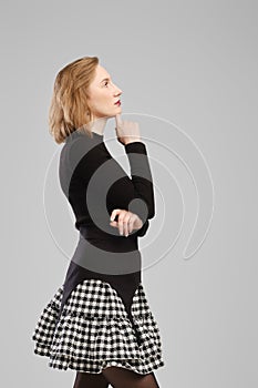 Young woman standing in profile in studio propping up chin and thinking
