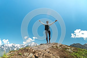 Young woman standing with raised hands with backpack on cliff`s edge and looking into a wide valley