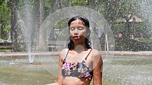 Young woman standing and relaxing in the swimming pool fountain shower.