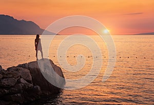 Young woman standing on the rock in the sea against mountains