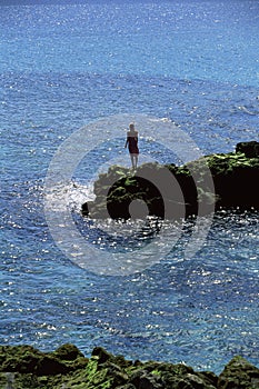 Young woman standing rocks, looking out to sea