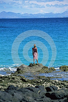 Young woman standing rocks, looking out to sea