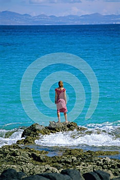 Young woman standing rocks, looking out to sea