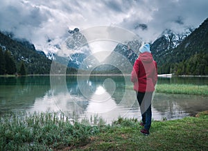 Young woman is standing on shore of lake in overcast rainy day