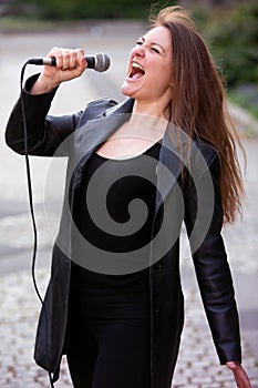 Young woman standing and singing with microphone outdoors