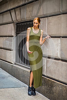 Young woman standing on street by wall in New York City, texting on cell phone