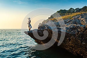 Young woman standing on the top of rock and looking at the seashore and sunset in Si chang island