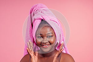 Young woman standing on towel tied on head with hands under chin in studio pink backhround