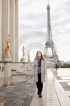 Young woman standing on Trocadero square near gilded statues and Eiffel Tower.