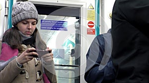 Young woman standing in tube carriage is typing text message on her mobile phone