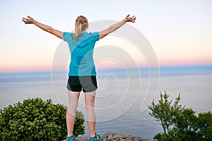 Young woman standing victoriously on a mountain top