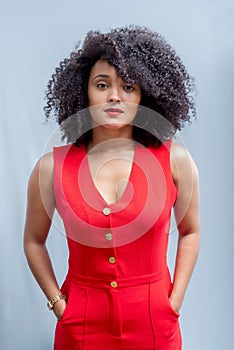 Young woman, standing, wearing a red outfit with curly hair posing next to a wooden stool