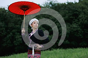 young woman standing wearing traditional thai culture lanna dress style and red umbrella holding hand in the natural garden,