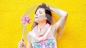 Young woman standing at yellow wall with pinwheel