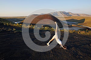 A young woman is standing in a yoga pose against the beautiful nature landscape of valley, volcanic lake and crater