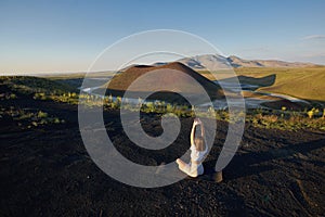 A young woman is standing in a yoga pose against the beautiful nature landscape of valley, volcanic lake and crater