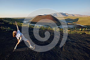 A young woman is standing in a yoga pose against the beautiful nature landscape of valley, volcanic lake and crater