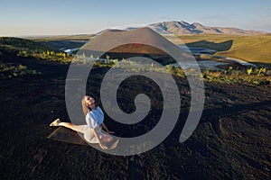 A young woman is standing in a yoga pose against the beautiful nature landscape of valley, volcanic lake and crater