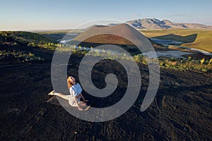 A young woman is standing in a yoga pose against the beautiful nature landscape of valley, volcanic lake and crater