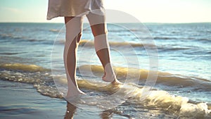 A young woman stands barefoot on the sandy seashore. The girl wets her feet close-up.