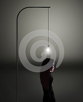 A young woman stands beneath a bright light bulb as she tries to come up with a new idea photo