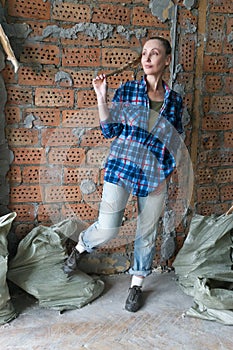 Young woman stands by a brick wall with bags of construction debris and thinks about repair