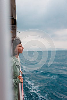 A young woman stands on the deck of a cruise ship and looks at the setting sun, close-up silhouette. A young beautiful brunette