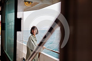 A young woman stands on the deck of a cruise ship and smiles. The girl smiles while traveling. A young beautiful brunette travels