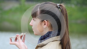 Young woman stands on the embankment of the river and talking on a cell phone. Girl speaking on smartphone outdoor in