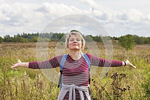 A young woman stands in a field with her arms outstretched to the sides and her eyes closed, enjoying the nature