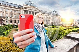 A young woman stands in front of the royal palace in Brussels and takes a selfie on her phone, Belgium